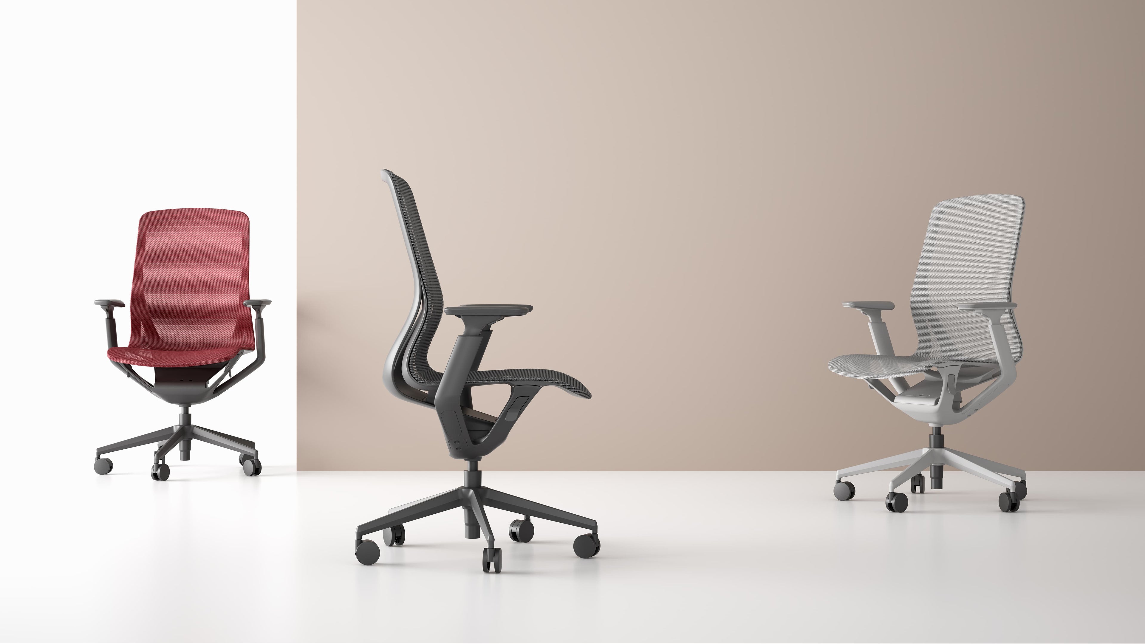 Three office chairs in red, black, and gray on a white floor with a beige wall background.