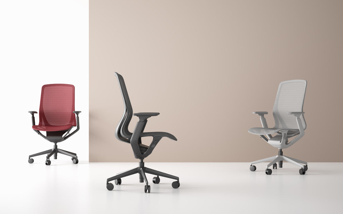 Three ergonomic mesh office chairs in black, coral red, and light grey, with lumbar support and adjustable height, without headrests